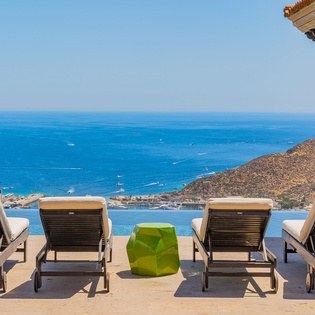Breathtaking Mediterranean coastline stretches endlessly before this elevated terrace, where comfortable loungers await beneath clear blue skies and warm sunshine.