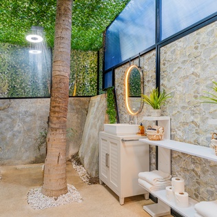 Step into your private tropical oasis where an outdoor shower cascades from above while you're surrounded by lush greenery and natural stone.