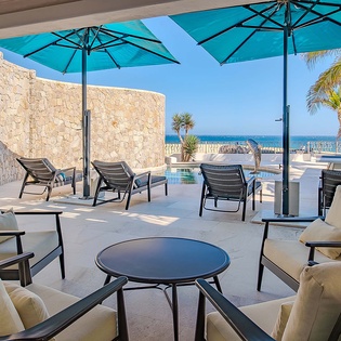 This covered terrace showcases elegant lounge seating with cushioned chairs, turquoise umbrellas, and a private pool, all framed by tropical palms and stunning ocean vistas beyond.