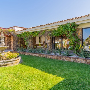 Mediterranean villa featuring stone architecture, lush gardens with decorative fountain, and spacious covered terrace areas.