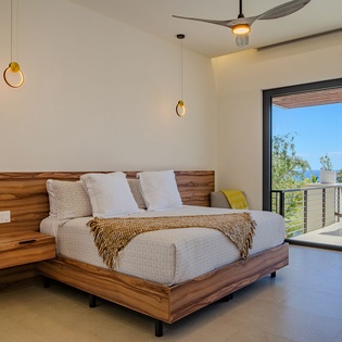 Unwind in your serene bedroom featuring warm wood tones and tropical views through floor-to-ceiling windows.