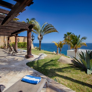 A coastal retreat with stunning panoramic ocean views, palm-framed lawns, and shaded terrace seating overlooking the sparkling blue water—perfect for peaceful seaside relaxation.