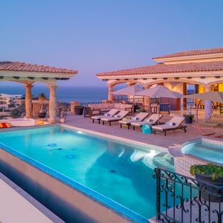 Stunning rooftop terrace with infinity pool, hot tub, and panoramic ocean views at dusk.