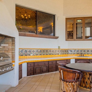 An outdoor patio space featuring a built-in grill, colorful tiled counters, and seating—ready for gatherings, casual meals, and relaxed evenings under the open sky.