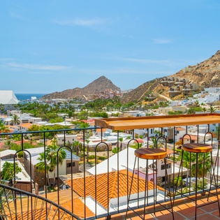 Elevated terrace overlooking a picturesque coastal town with mountain and sea views. Features bar seating and partial shade for outdoor relaxation.
