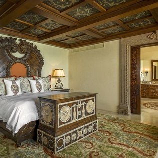 Rest in luxury within this ornate bedroom featuring intricate carved details, a coffered ceiling, and handcrafted furnishings that transport you to old-world elegance.