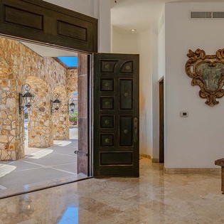 Grand carved wooden doors open to a sun-drenched stone courtyard, while elegant wall art and polished marble floors set a refined, welcoming tone.