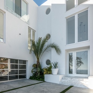 Modern white facade with tropical plants and glass entrance creates a welcoming arrival experience.