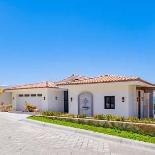 Beautiful Mediterranean-style villa with terracotta roof tiles surrounded by lush tropical landscaping and palm trees.