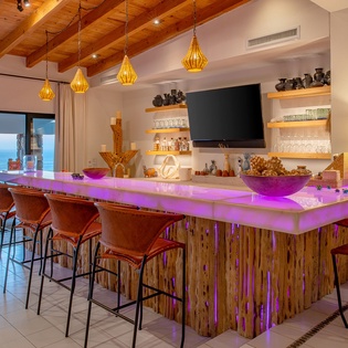 Gather around this stunning illuminated bar with ocean views, where warm wood beams and glowing pendant lights create your perfect evening retreat.