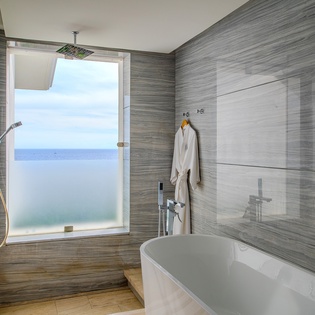Unwind in your spa-like bathroom featuring a luxurious soaking tub and rainfall shower, all while gazing out at stunning sea views.