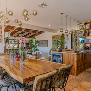 Gather around this stunning live-edge dining table where natural wood warmth meets modern design. The open kitchen's stylish shelving and ambient globe lighting create an inviting space for shared meals and conversation.