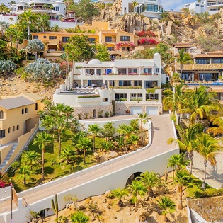 This stunning hillside community showcases terraced villas nestled into the rocky coastline, featuring lush tropical landscaping, sandy pathways, and vibrant Mediterranean-style architecture.