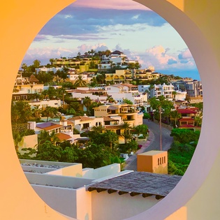 Hillside homes cascade across the tropical landscape through this striking circular window frame, showcasing the vibrant neighborhood at golden hour.
