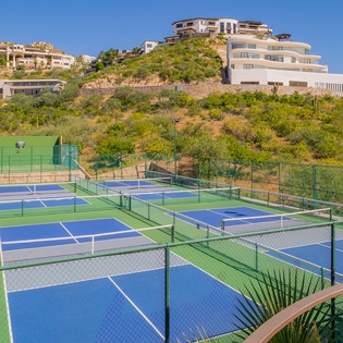 Multiple tennis courts nestled in hillside setting with luxury homes and lush vegetation creating a scenic recreational complex.