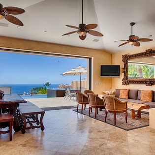 Your open, tropical living space frames the azure sea and lush palms, with warm tones, plush seating, and elegant details inviting relaxation and coastal charm.