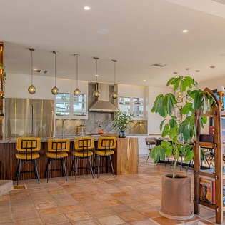 Step into this sun-soaked open kitchen with a stylish marble island, vibrant yellow bar stools, and lush greenery creating a fresh, welcoming vibe for your stay.