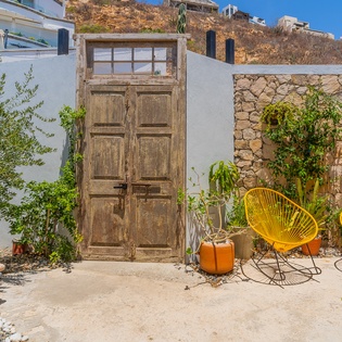 Charming private courtyard with vibrant yellow seating, rustic wooden doors, and lush greenery—a peaceful spot to unwind under the sun.