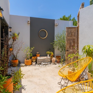 A charming inner courtyard with colorful seating and potted plants surrounds this tranquil outdoor space, offering a peaceful retreat under sunny skies.