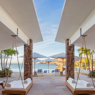 A covered patio with stone columns and hanging daybeds frames stunning ocean views. Enjoy the breeze from the shade as you relax in this open-air sanctuary.