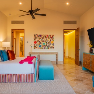 Unwind in your vibrant bedroom featuring colorful artwork, a striped headboard, and comfortable seating beneath a cooling ceiling fan.