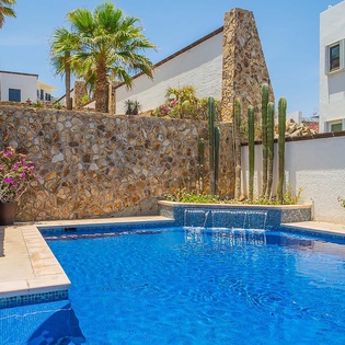 Your private oasis awaits—sparkling blue water, gentle fountain sounds, desert cacti, and palm trees framing a sun-drenched poolside perfect for lazy afternoons.