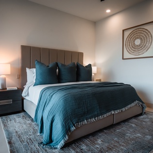 Sink into this plush queen bed adorned with rich teal linens and thoughtful decor for your perfect night's rest.