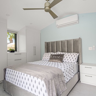Sink into comfort in this serene bedroom featuring a plush upholstered bed, ample storage, and cooling ceiling fan for your perfect retreat.