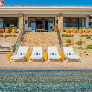 This stunning Mediterranean villa features stone architecture, colorful gardens, and a sparkling pool with loungers for perfect outdoor relaxation.