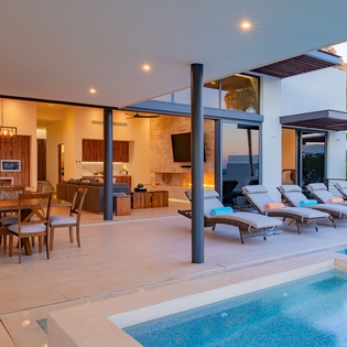 Your seamless indoor-outdoor living flows from modern kitchen to poolside loungers, perfect for entertaining under warm evening lights.