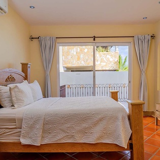 Wake up in this peaceful bedroom with its inviting wood furnishings and warm terracotta floors. Through your window, glimpse stone walls and tropical greenery in the distance. Cool off easily with air conditioning overhead.