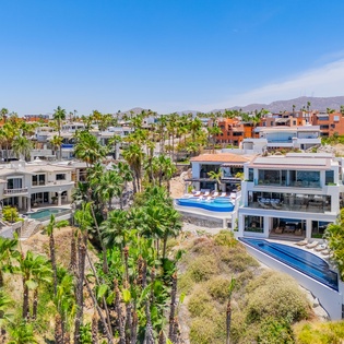 Aerial view showcases luxury beachfront properties with pools nestled among palm trees in a tropical coastal community.