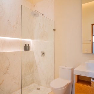 Indulge in your private spa-like bathroom with elegant marble walls, rainfall shower, and warm ambient lighting for complete relaxation.