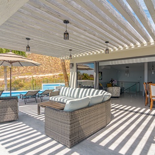 Relax in your stylish covered terrace where wicker seating and dramatic ceiling beams create perfect poolside comfort.
