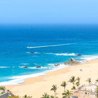 Pristine golden beach meets crystal-clear turquoise waters, with dramatic rock formations and swaying palms creating a stunning coastal paradise.