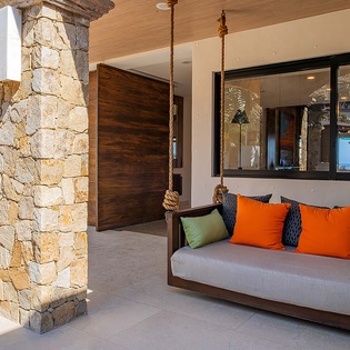 Swing gently in this charming covered terrace, where vibrant cushions invite you to relax and soak in ocean glimpses framed by elegant stonework and modern design.