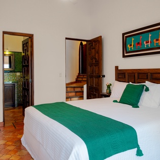 Relax in your charming bedroom with vibrant green accents, handcrafted wooden headboard, and colorful local artwork creating an authentic cultural atmosphere.