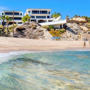 Modern beachfront properties overlook pristine sandy shores and crystal-clear turquoise waters with gentle waves.