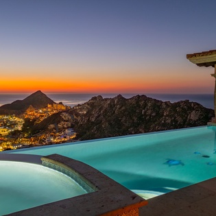 Stunning infinity pool overlooks coastal mountains and city lights during golden sunset. Perfect evening setting with hot tub.