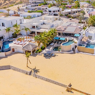 Stunning beachfront property with multiple pools and tropical landscaping set within a tranquil coastal community, surrounded by palm trees and neighboring residences.