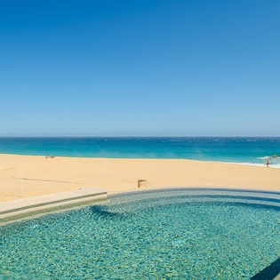 A pristine beachfront property offering a private pool with golden sands and turquoise waters just steps away under endless blue skies.