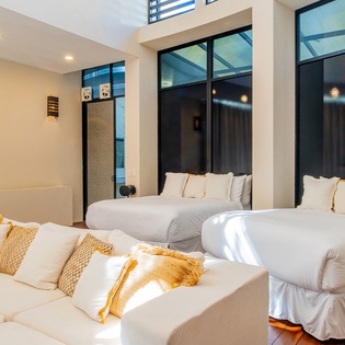 Your modern bedroom features two comfortable beds with crisp white linens and golden accents, flooded with natural light from floor-to-ceiling windows.