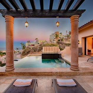 A private pool and patio framed by rustic columns capture stunning ocean and hillside views at twilight. Relax on plush loungers as the sky shifts from blue to rose, with warm lanterns glowing overhead.