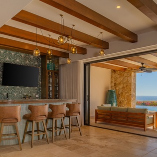Step into your stunning open-concept bar and lounge where exposed beams frame panoramic ocean views from your private terrace.