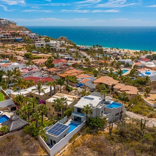 Stunning aerial view of a coastal resort community featuring luxury villas with private pools nestled between hillside and pristine beach.