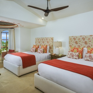 Unwind in your elegant twin bedroom featuring plush beds with vibrant linens and stunning ocean views from arched windows.