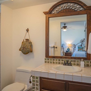 Your private bathroom features a charming tiled vanity and ornate woodwork, with the bedroom visible just beyond, creating a warm, connected retreat for your stay.