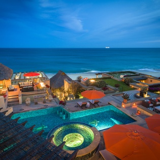 Spectacular beachfront villa complex featuring illuminated pool, hot tub, and luxury outdoor spaces with ocean views.