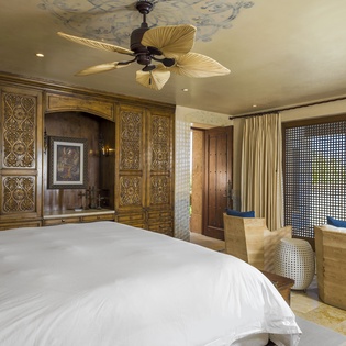 Relax in your luxurious bedroom featuring handcrafted woodwork, tropical ceiling fan, and comfortable seating area with stunning views.
