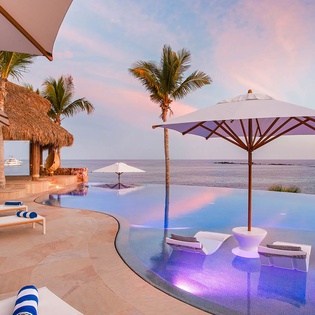 A stunning infinity pool merges with ocean views as sunset paints the sky in soft pastels, creating a serene paradise where relaxation meets tropical luxury.